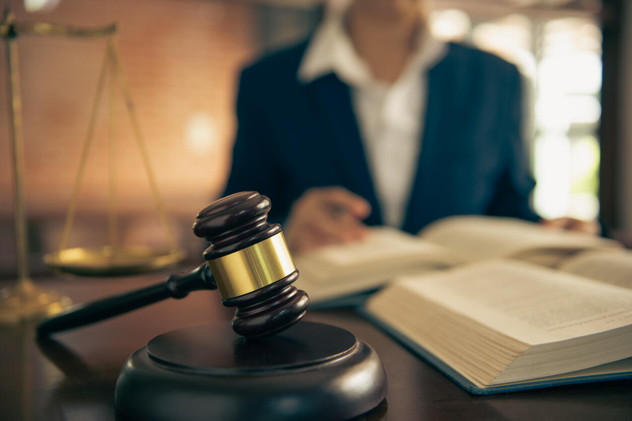 Close-up of a gavel and legal scales, with a blurred lawyer reviewing a book, symbolizing court decisions in divorce cases.