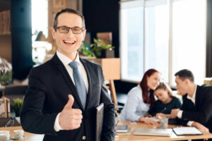 Smiling lawyer giving a thumbs-up in an office, with a family in the background, representing the positive outcome of child support enforcement.