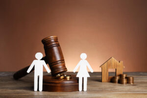 Wooden gavel, paper cutouts of a man and woman, wedding rings, and a house model, symbolizing the enforcement of visitation rights in family law.