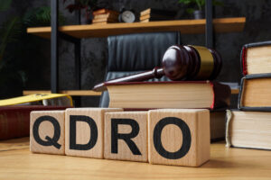 Wooden blocks spelling 'QDRO' with a gavel and law books, symbolizing the legal process of a Qualified Domestic Relations Order in divorce cases.