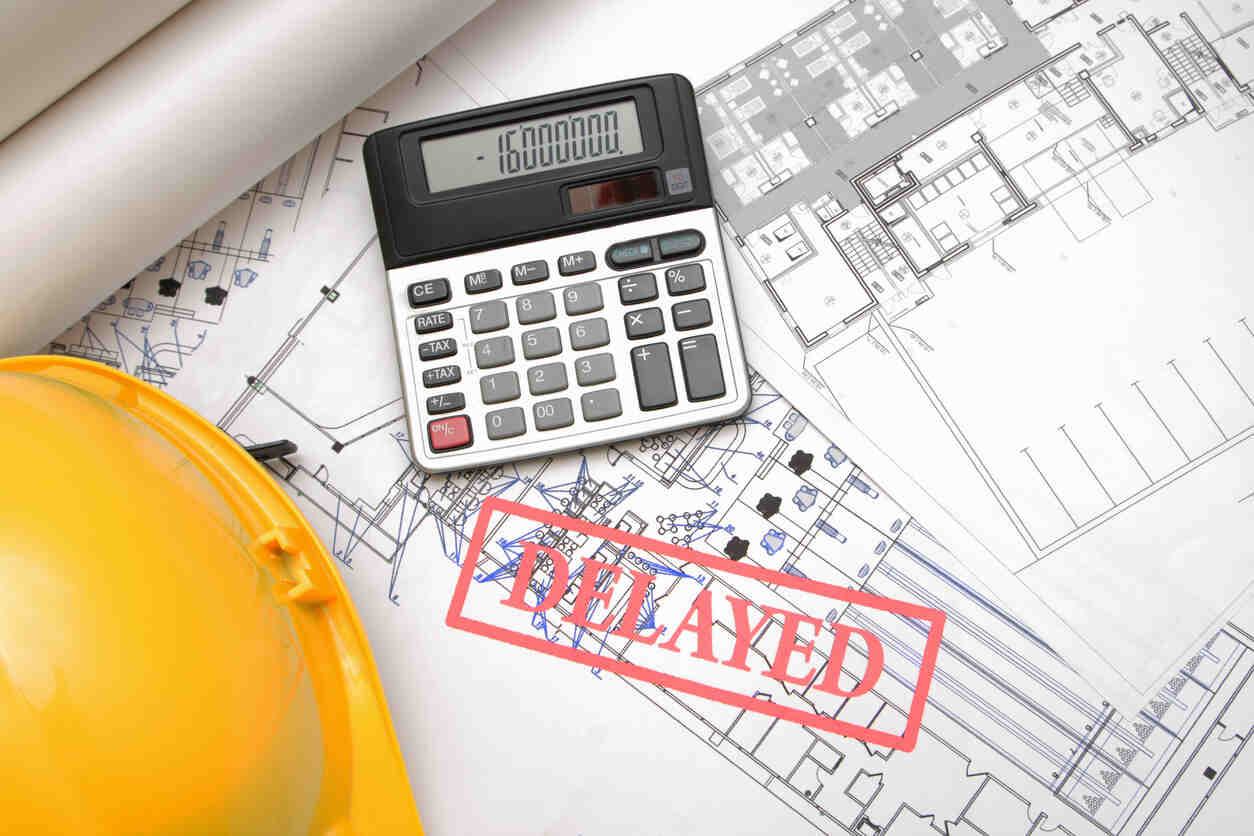 Construction blueprints with a calculator showing a high number and a red 'DELAYED' stamp, symbolizing project delays.